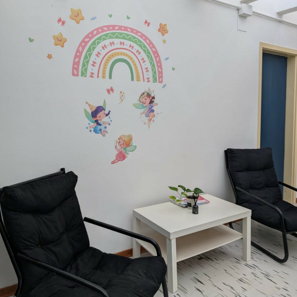 due sedie scure, un tavolino e dei disegni sul muro bianco