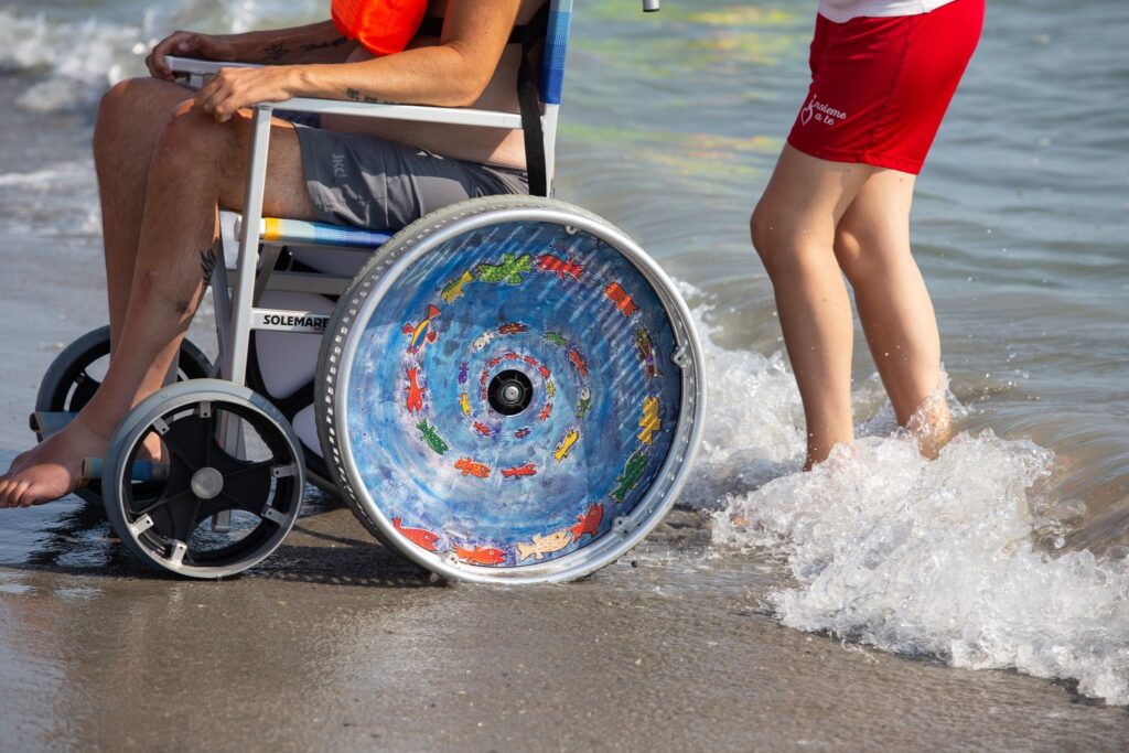 carrozzina con disabile e accompagnatore sulla battigia
